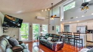 A spacious living room with a leather sofa, a flat-screen TV mounted on the wall, and a ceiling fan. - Private Dock + Lake View: Spacious Ozarks Retreat (Osage Beach)
