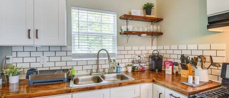 A kitchen with white cabinets, a wooden countertop, a double sink, and a stove.