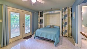 A bedroom with a bed, a ceiling fan, a window with curtains, and a door with a mat. - Walk to Padre Beach: Studio w/ Hot Tub Access (Corpus Christi)