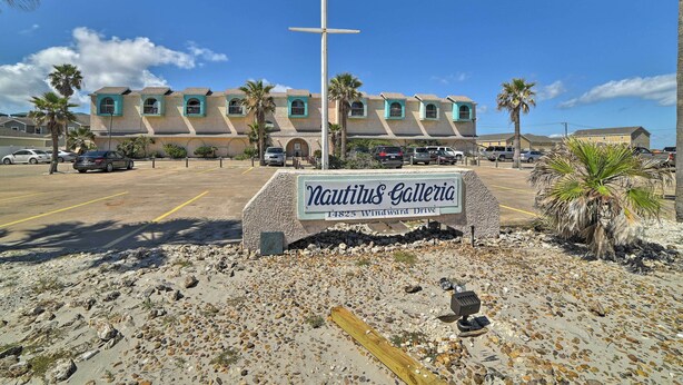 A building with a sign reading "Nautilus Galleria" at 14825 Windward Drive, featuring a cross, palm trees, and a parking lot. - Walk to Padre Beach: Studio w/ Hot Tub Access (Corpus Christi)
