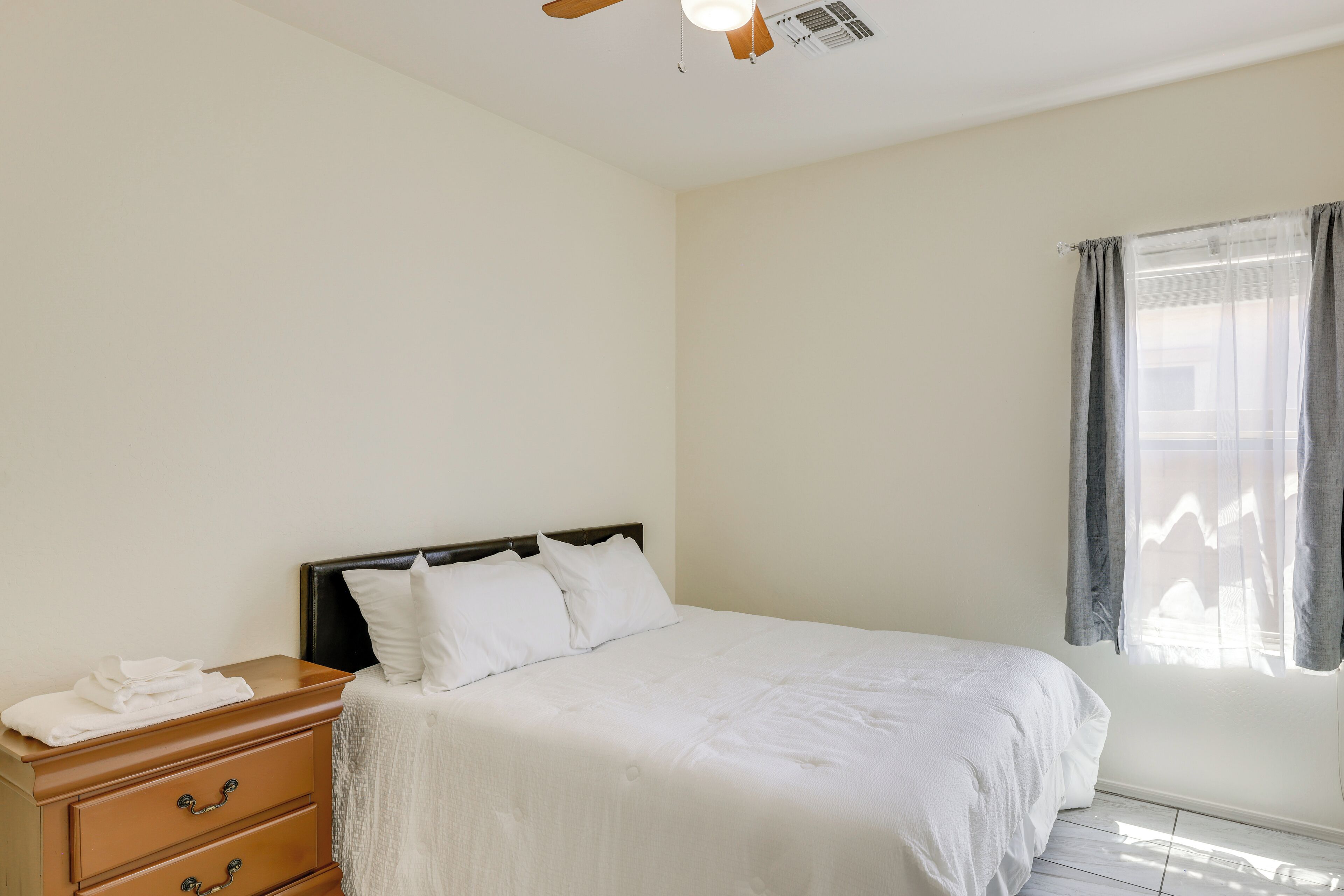 A bedroom with a bed, a nightstand, a ceiling fan, and a window with curtains.