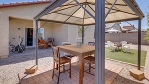 Une terrasse extérieure avec une table et des chaises en bois, un espace salon couvert et un sol en gravier.