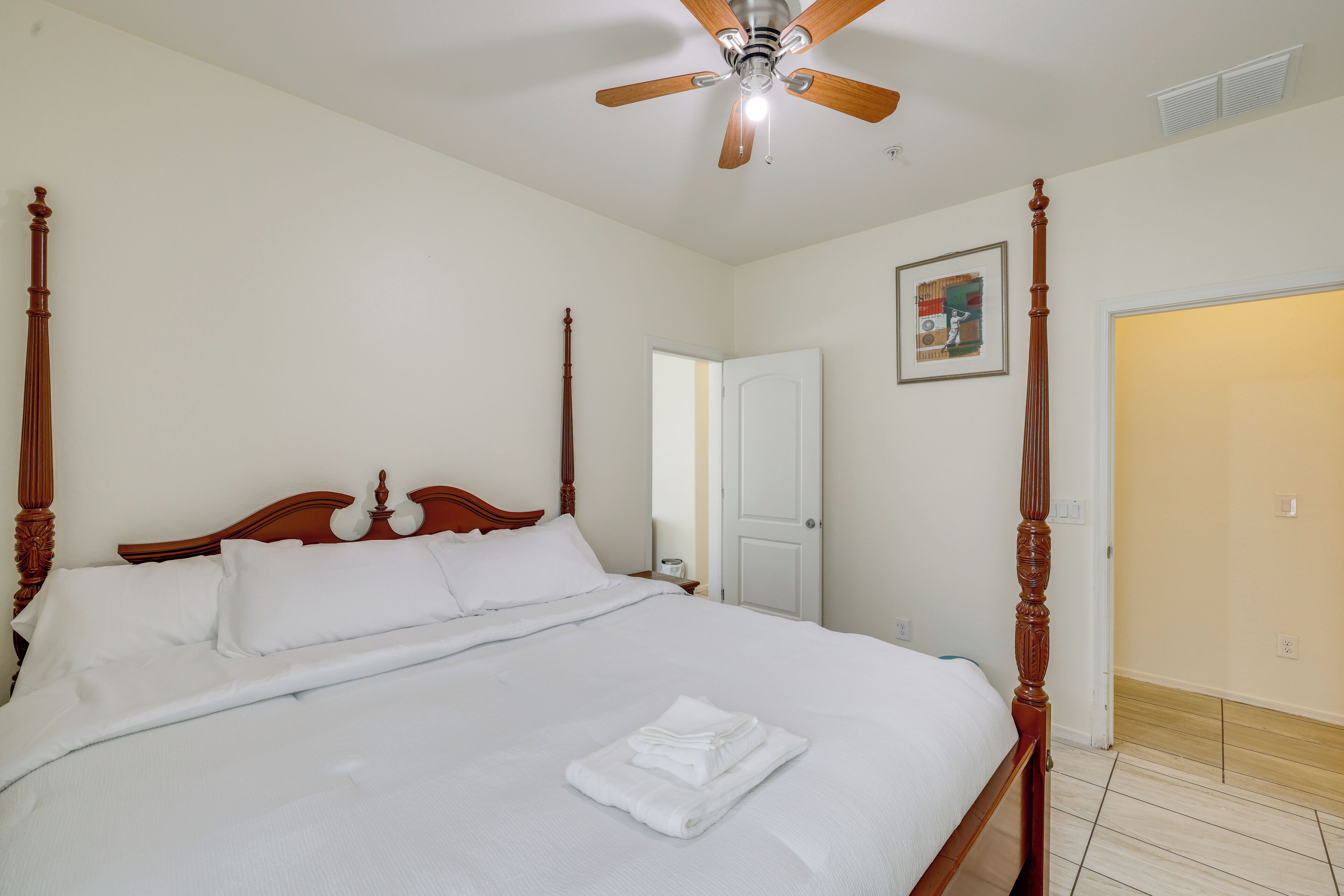A neatly made bed with a wooden headboard, a ceiling fan, and a door in the background.