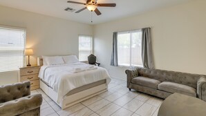 Une chambre à coucher comprenant un lit, un canapé, une chaise, un ventilateur de plafond et deux fenêtres avec des rideaux.