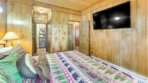 Ein Zimmer mit Holzwänden, einem Bett, einem Fernseher und einem zur anderen Räumlichkeit führenden Gang.