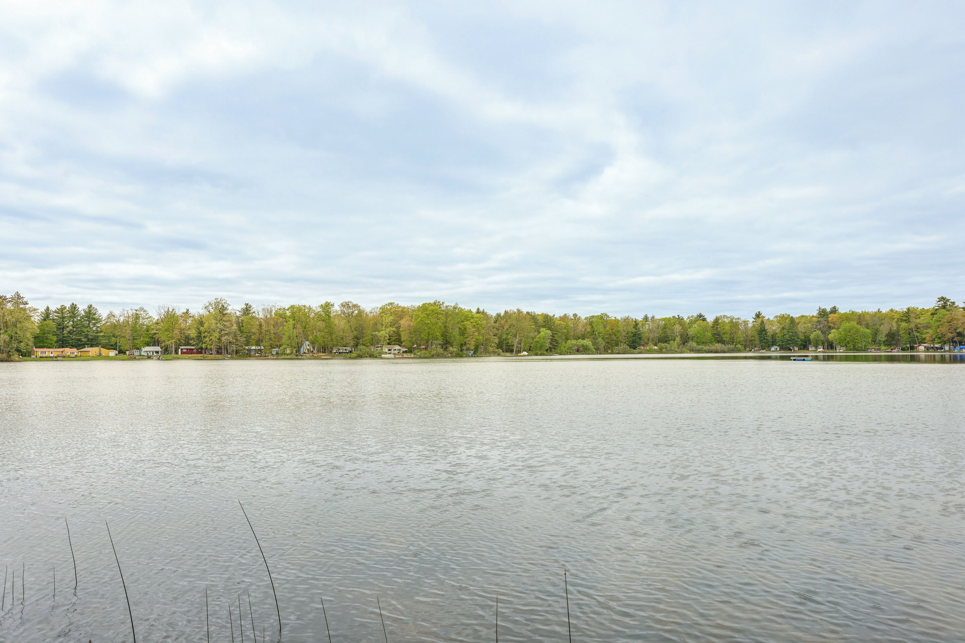 A calm lake with a forested shoreline and buildings in the background.