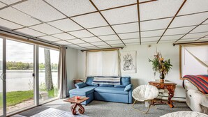 A living room with a sectional sofa, a round chair, a small table, and a large window overlooking a body of water. - Lakefront Group Getaway w/ Dock in Baldwin! (Baldwin)