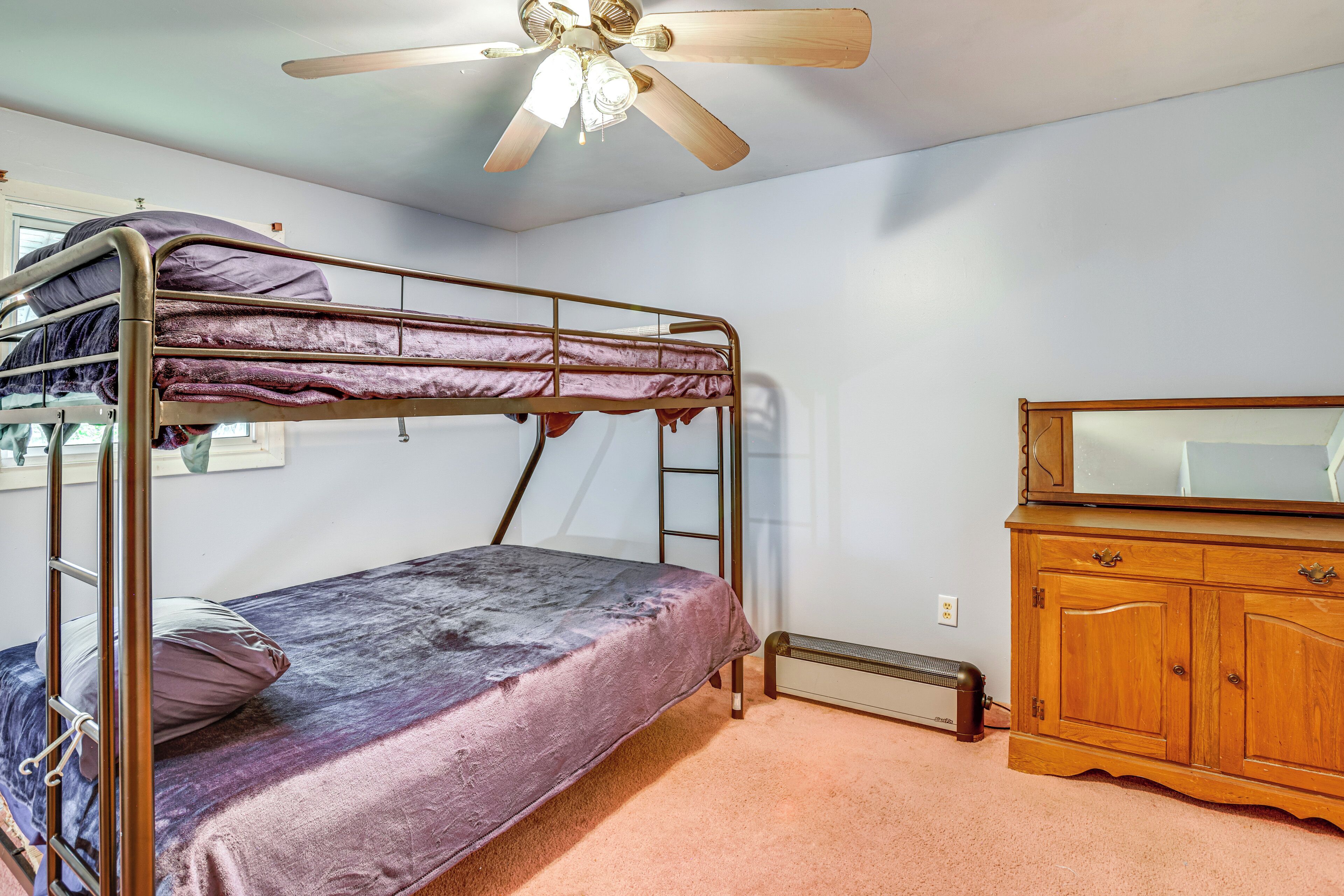 A bunk bed with a ceiling fan, a dresser, and a radiator in a room with light-colored walls.