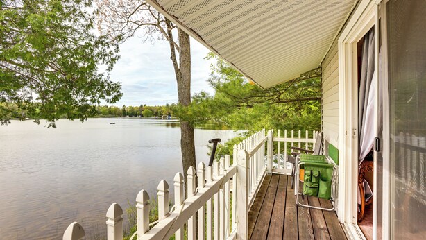 A wooden deck with a white picket fence overlooking a calm lake. - Lakefront Group Getaway w/ Dock in Baldwin! (Baldwin)