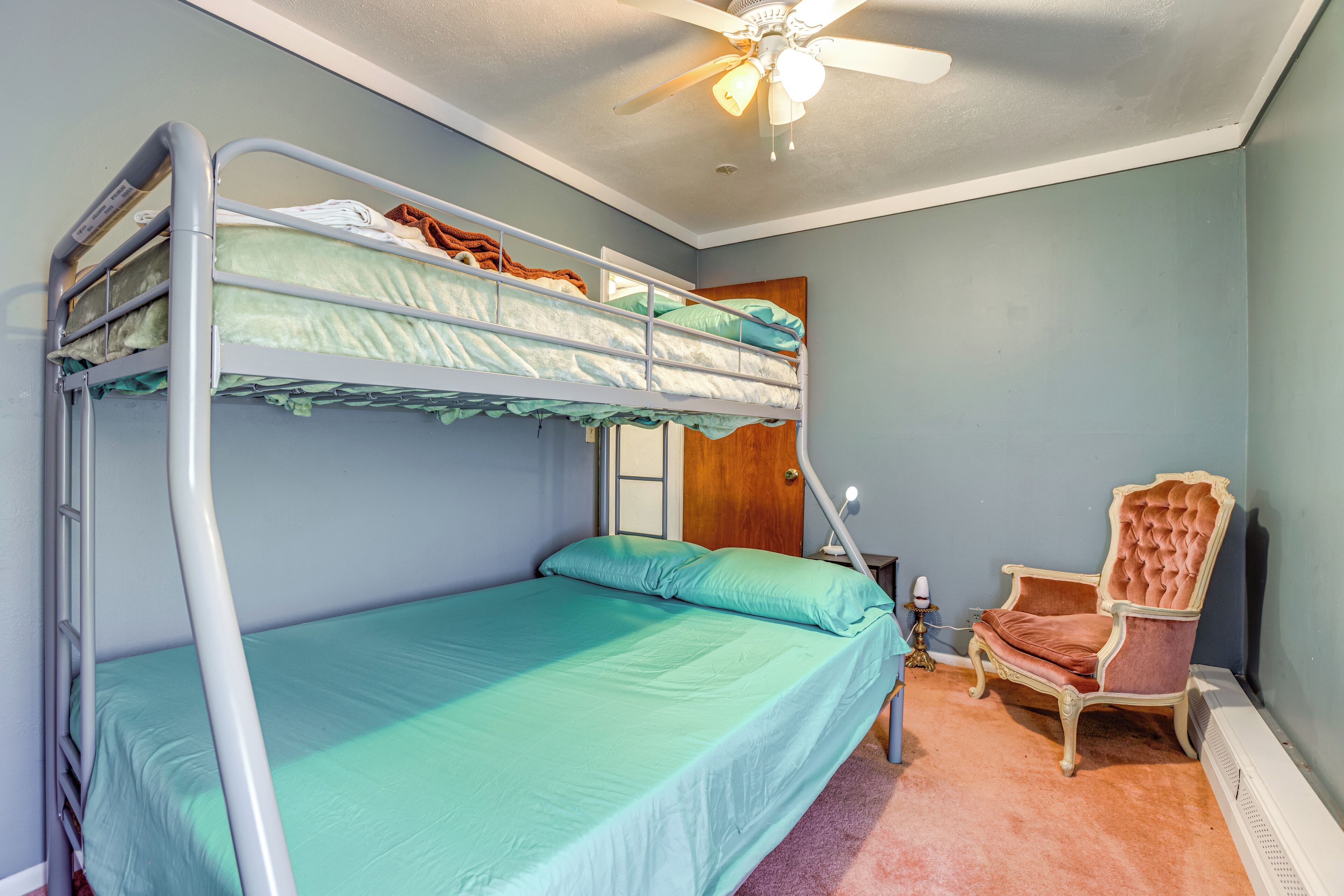 A bunk bed room with a ceiling fan, a wooden door, a chair, and a nightstand.
