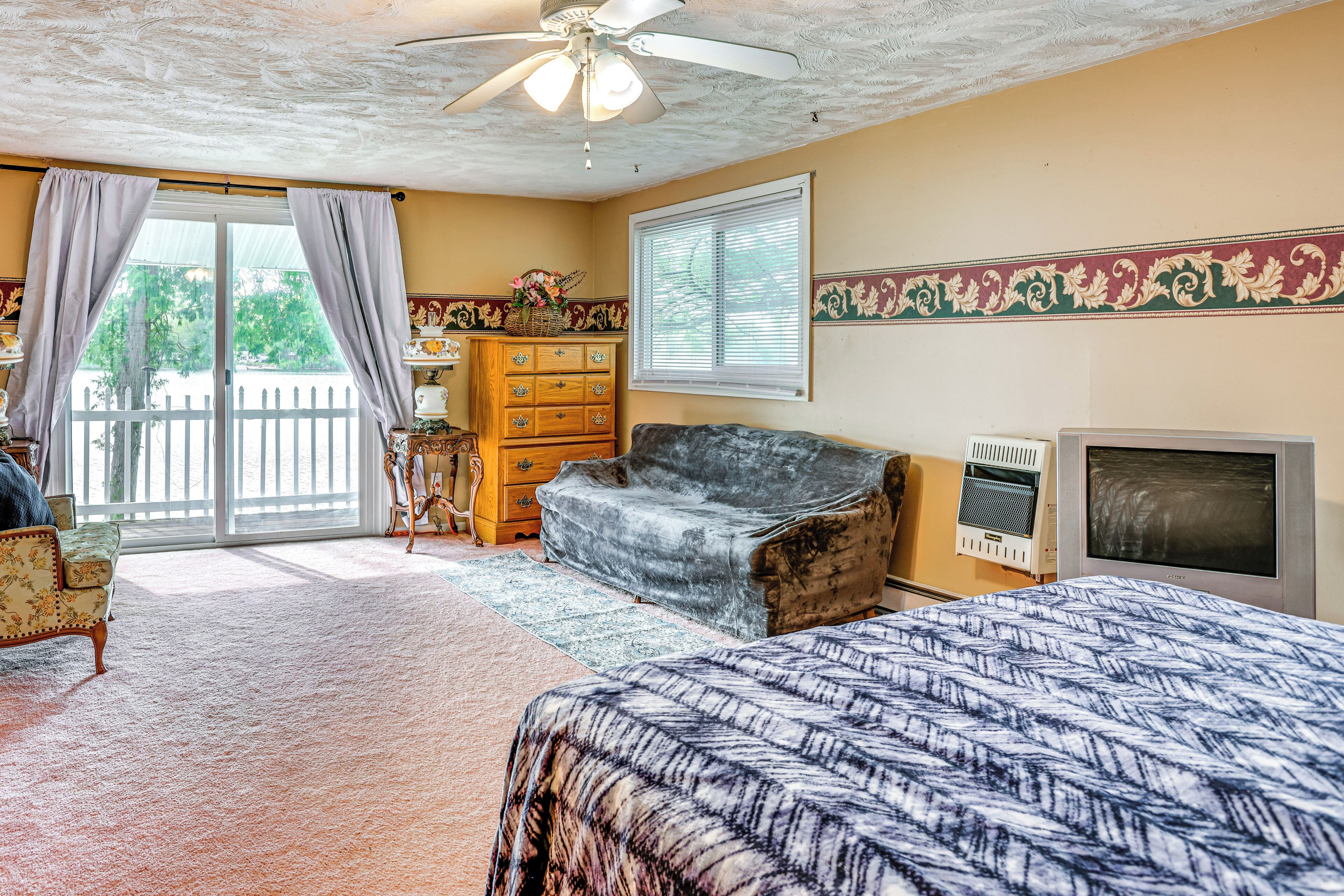 A room with a bed, a dresser, a chair, a television, and a ceiling fan.