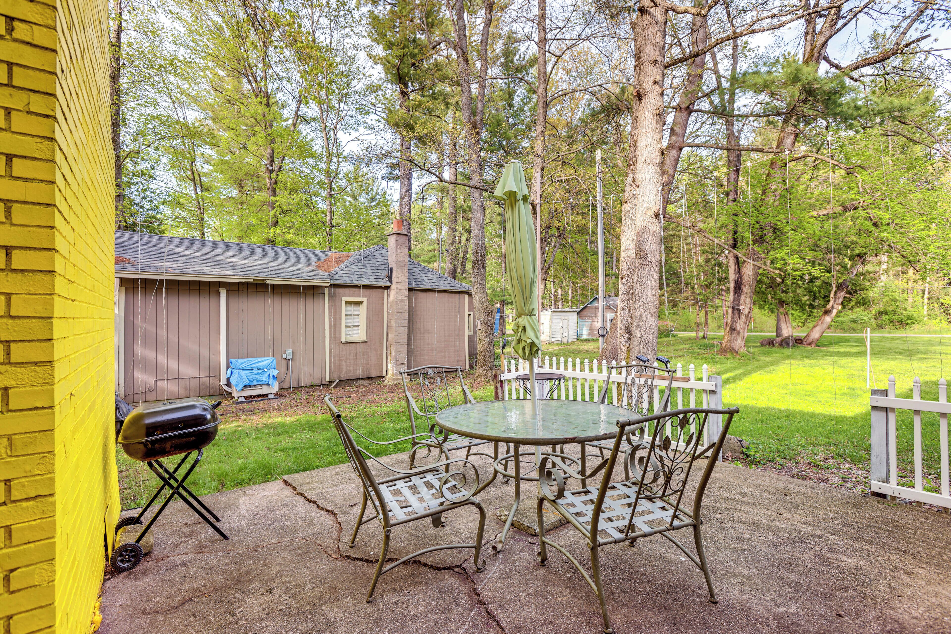 A patio with a metal table and chairs, a grill, and a white picket fence.