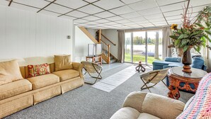 A spacious living room with a large window, a sofa, a chair, and a coffee table. - Lakefront Group Getaway w/ Dock in Baldwin! (Baldwin)