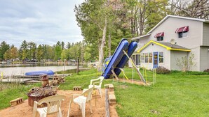 A house with a slide, a pond, and chairs in the yard. - Lakefront Group Getaway w/ Dock in Baldwin! (Baldwin)