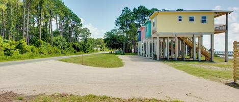 A coastal property with a multi-level house on stilts, a paved driveway, and a road curving to the left.