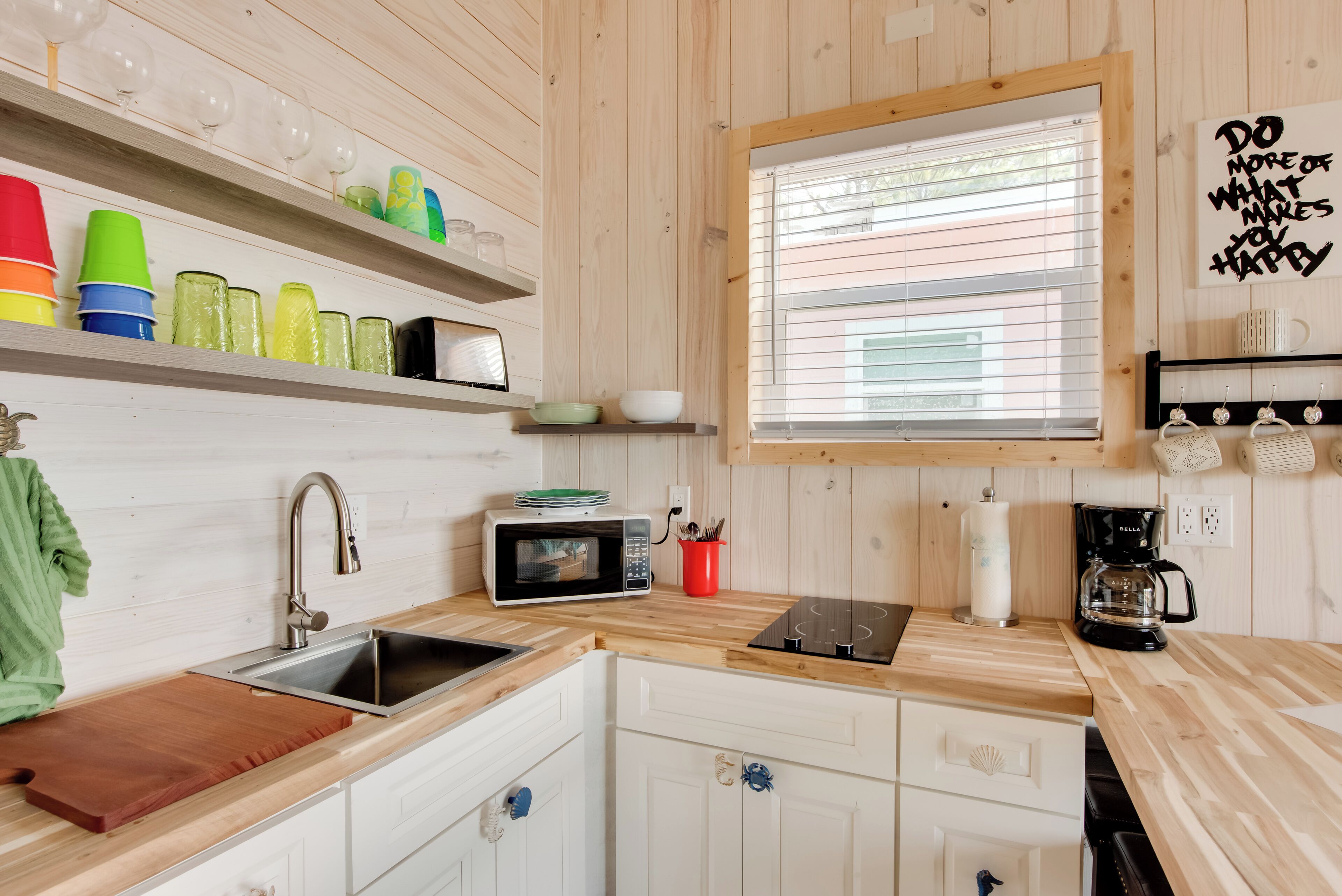 A kitchen with wooden cabinets, a sink, a microwave, a coffee maker, and a window with blinds.