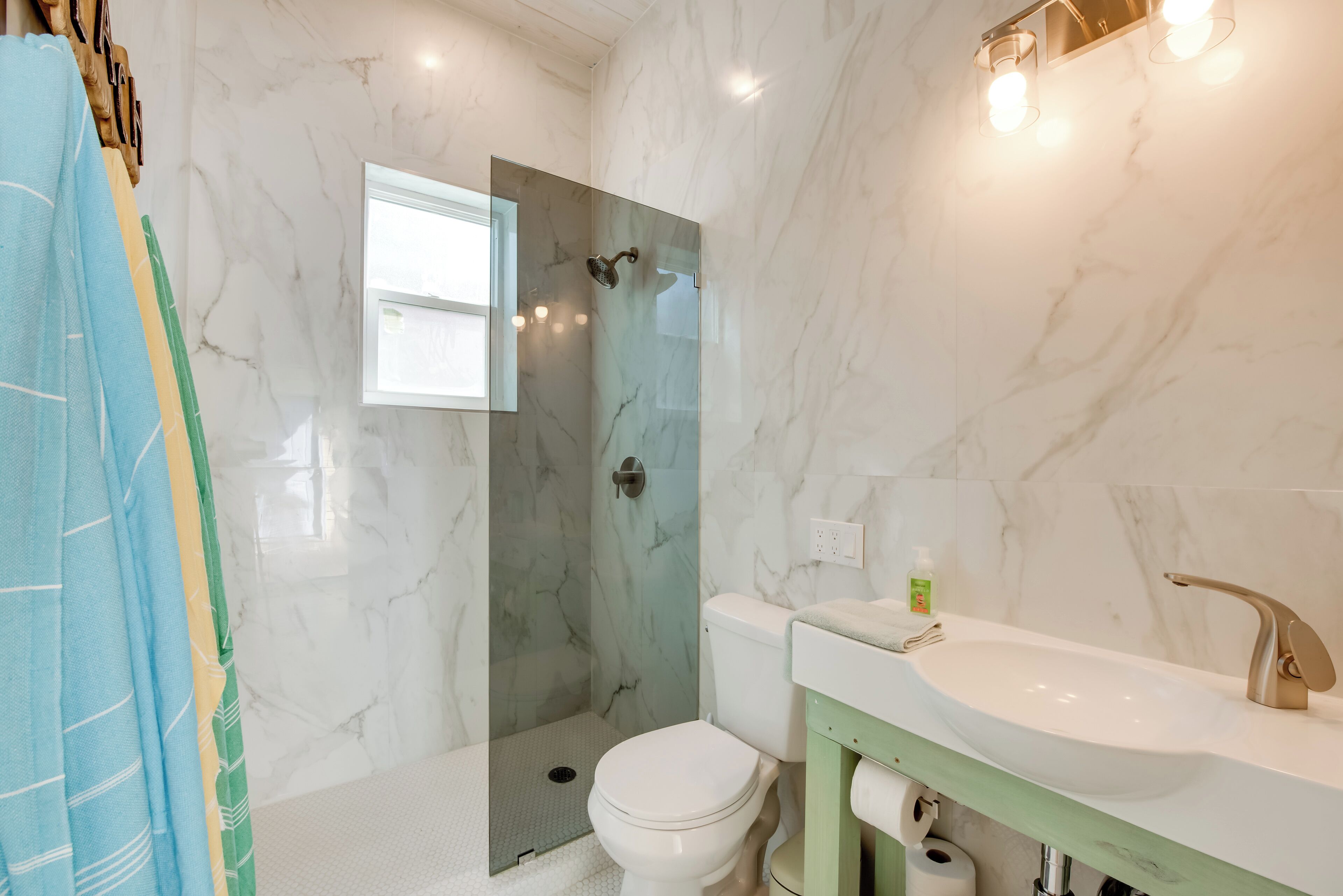 A bathroom with a glass shower enclosure, a white toilet, and a sink with a green vanity.