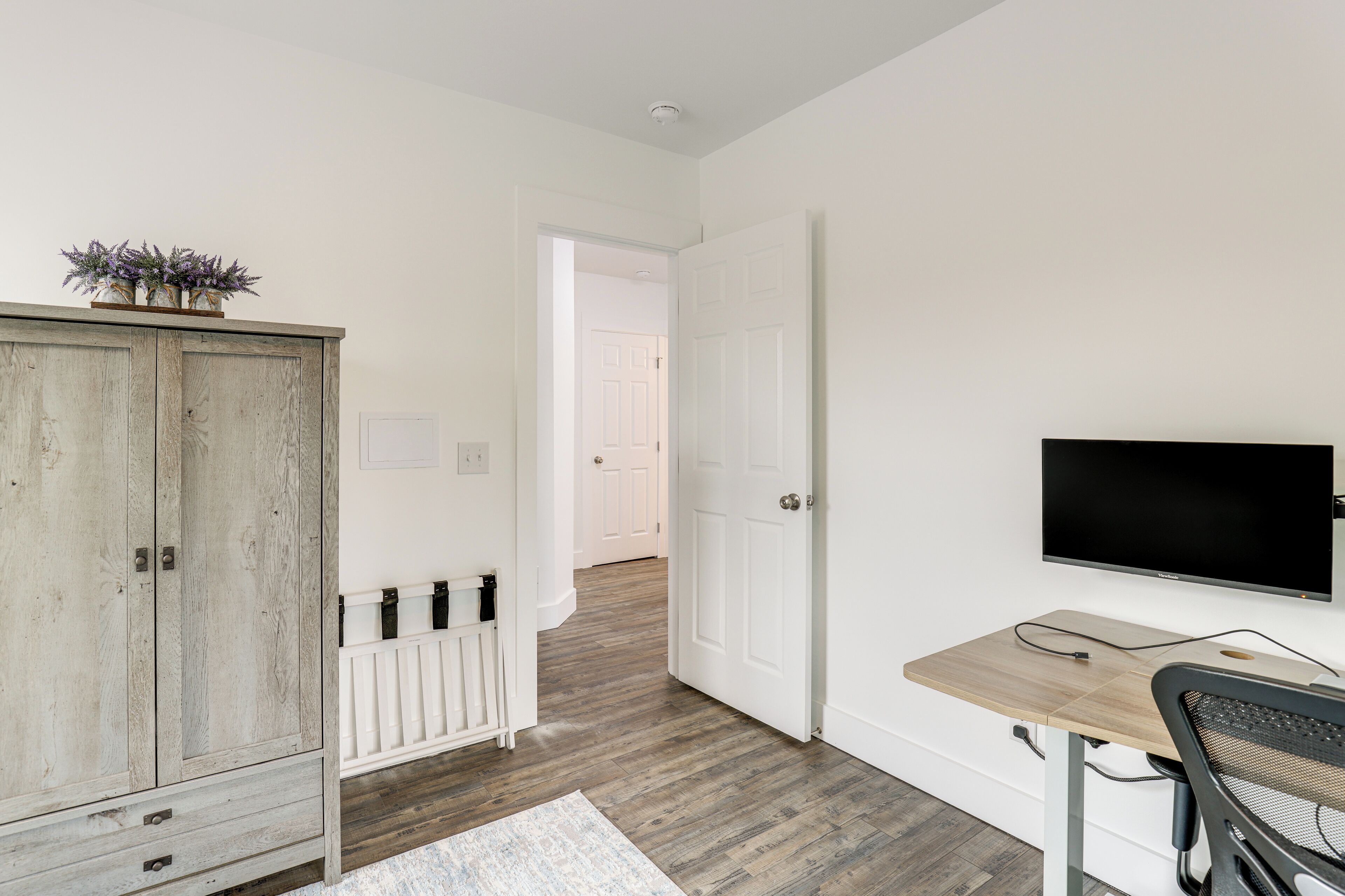 Ein Zimmer mit einem Holzkasten, einem Schreibtisch mit Computer und einem Fernseher an der Wand.