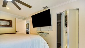 Une chambre d’hôtel dotée d’un grand lit, d’un téléviseur à écran plat fixé au mur, d’un miroir au-dessus du lit et d’un dressing.