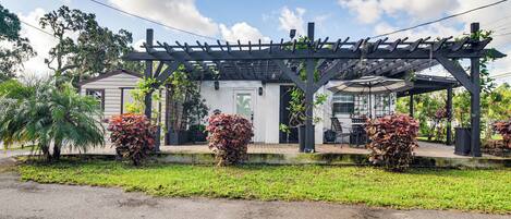 A building with a covered patio area, a small garden with various plants, and a clear sky.