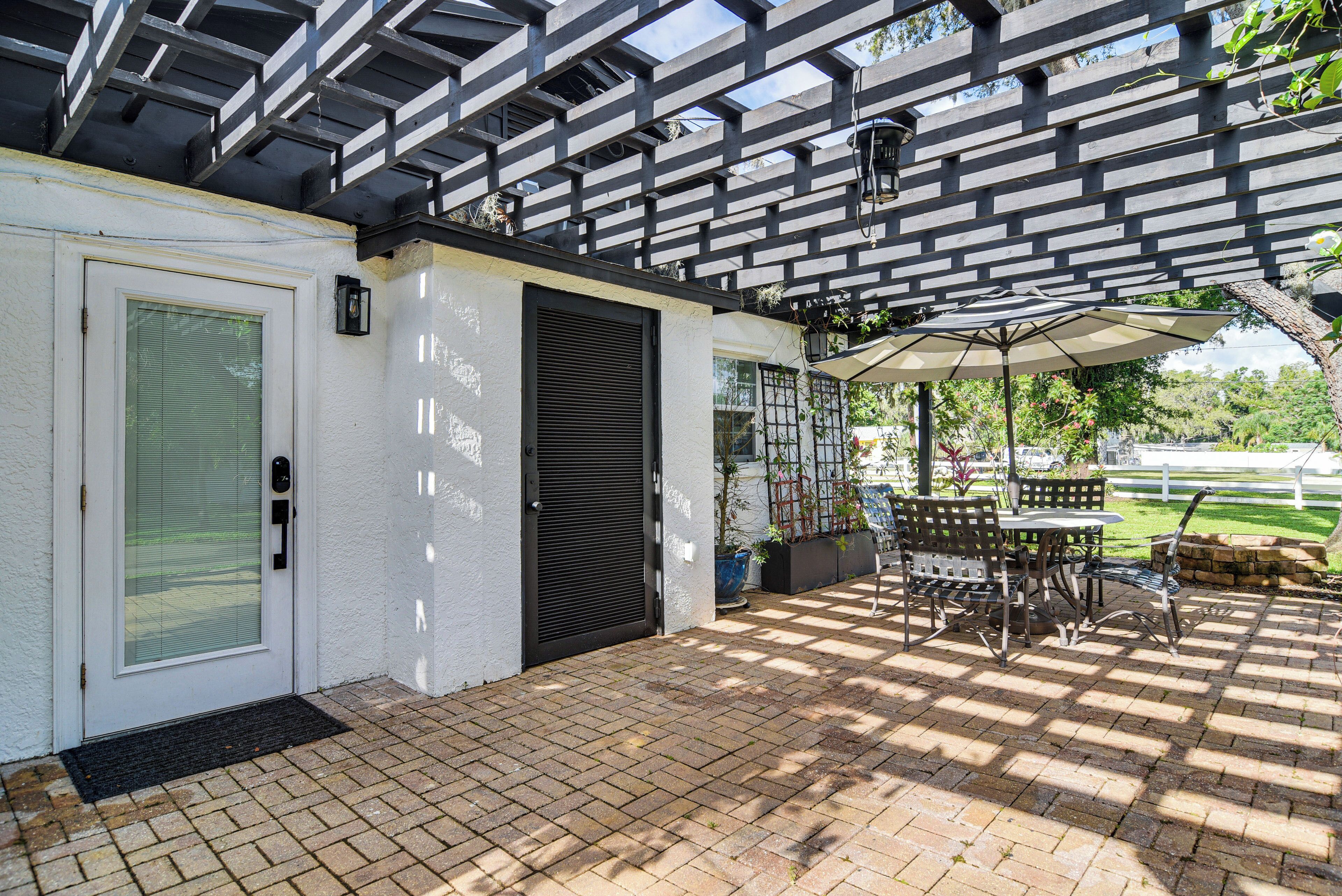 A covered patio with a brick floor, outdoor furniture, and a pergola overhead.