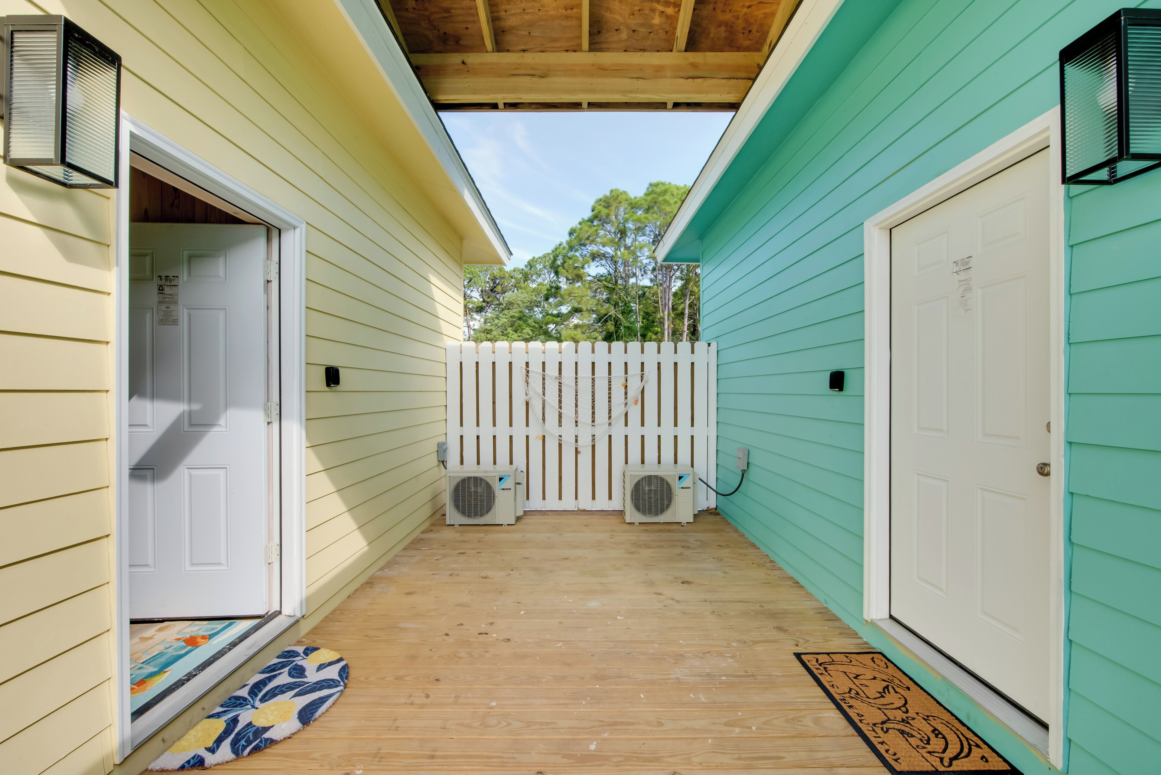A covered porch with a wooden floor, a white picket fence, and two air conditioning units.