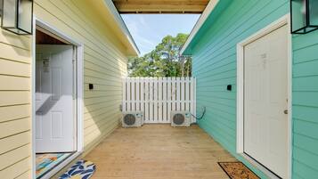 A covered porch with a wooden floor, a white picket fence, and two air conditioning units.