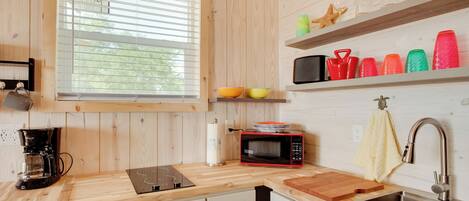 A modern kitchen with wooden cabinetry, a black coffee maker, a microwave, a cutting board, and a stainless steel sink.