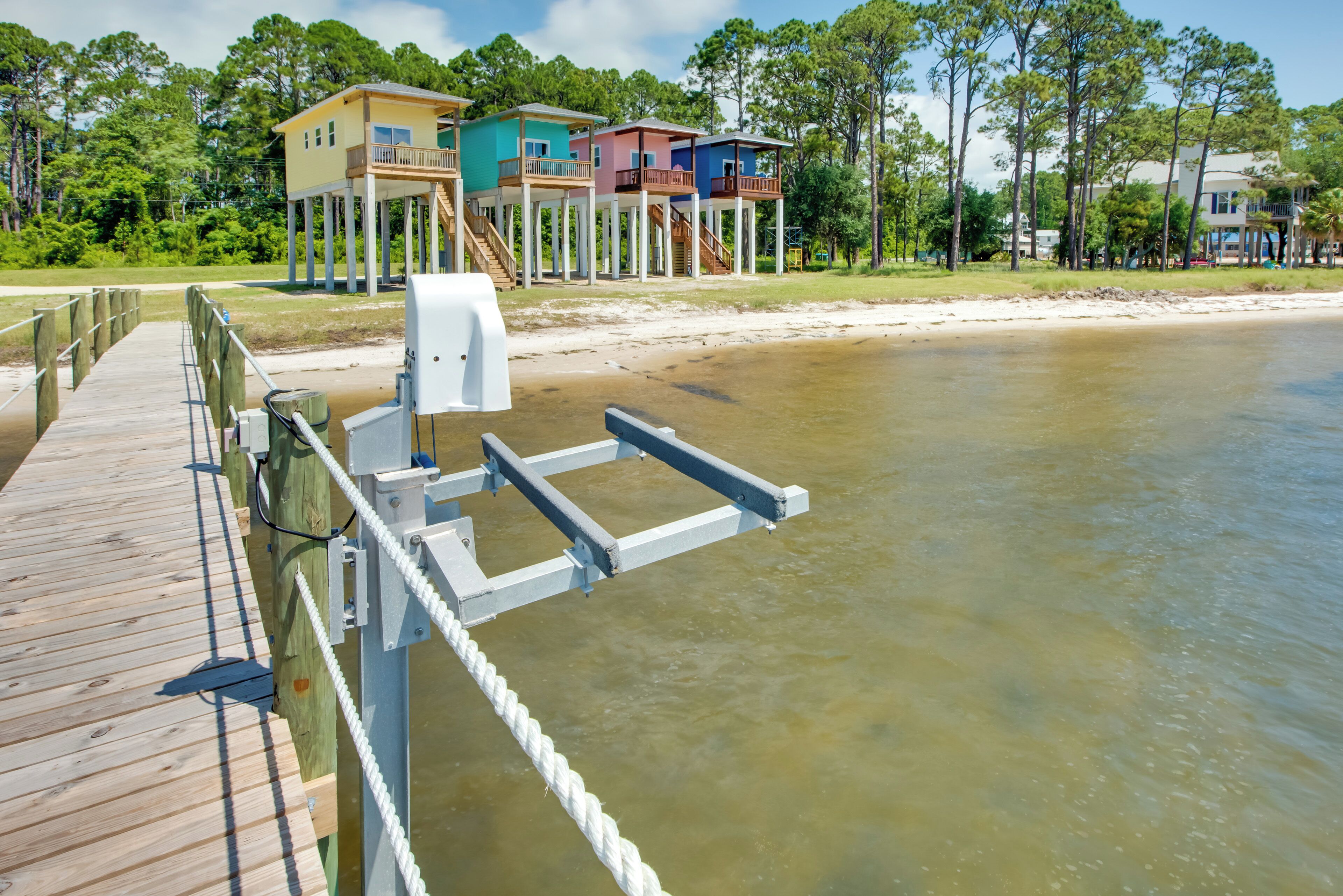 A wooden pier leading to a beach house with multiple levels, a dock, and a clear view of the water.