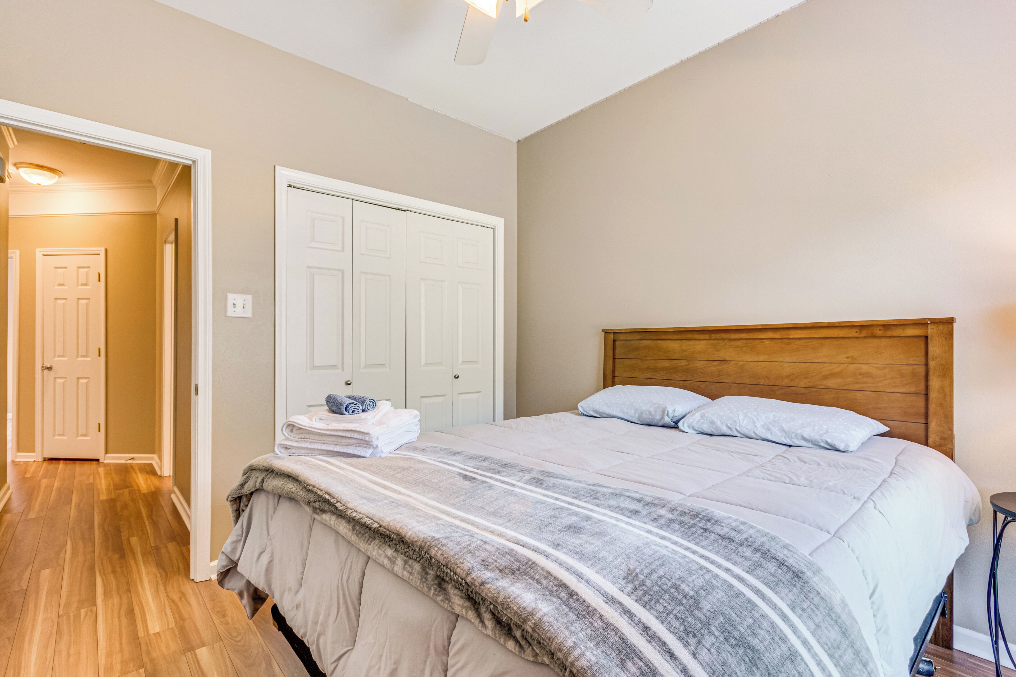 Une chambre à coucher avec une tête de lit en bois, un grand lit recouvert d’une couverture rayée grise et blanche, une porte blanche et un plancher en bois.