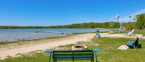 A lakeside park with a bench, picnic tables, and a fire pit.