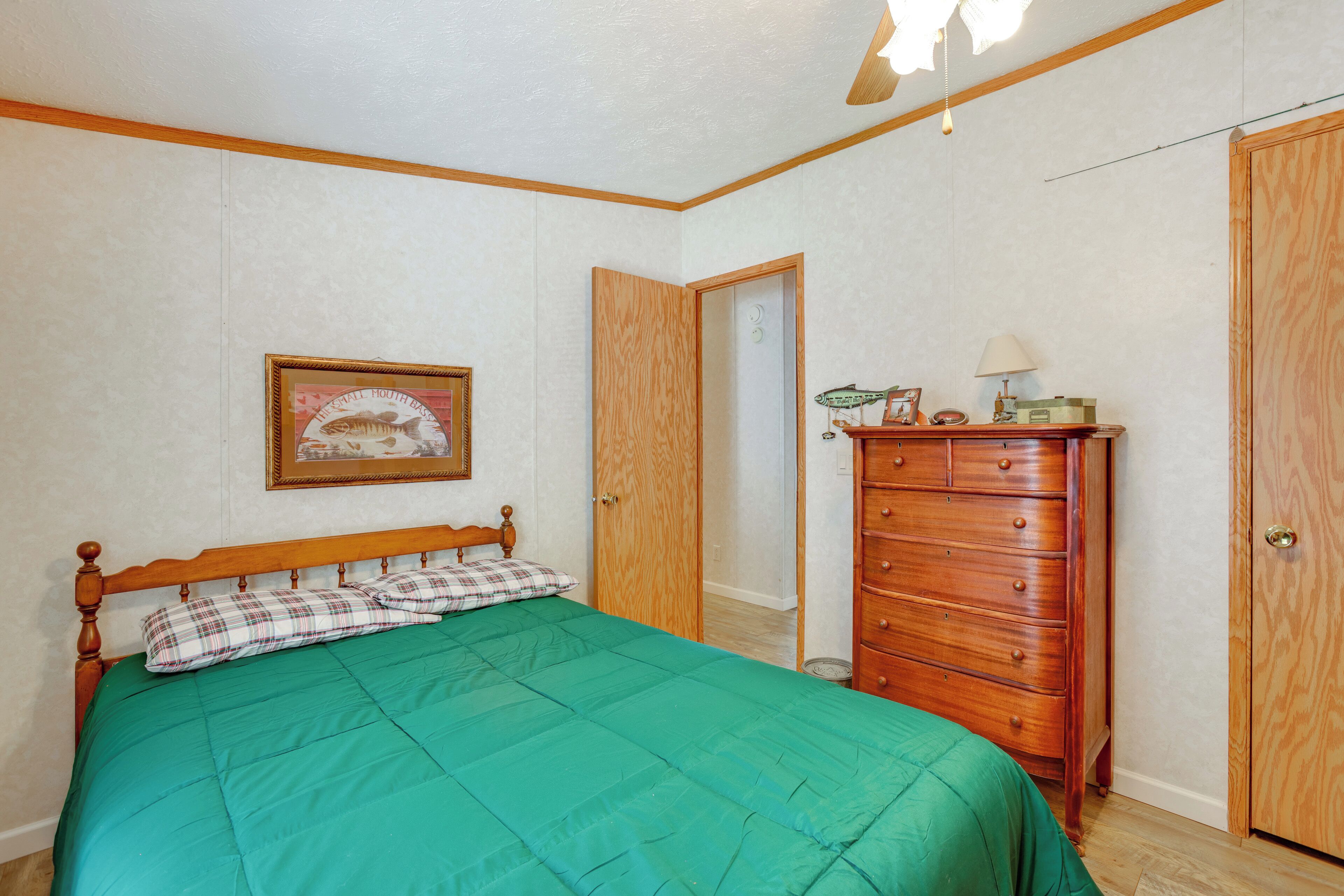 Une chambre à coucher avec un lit, une commode, une porte et un tableau encadré au mur.