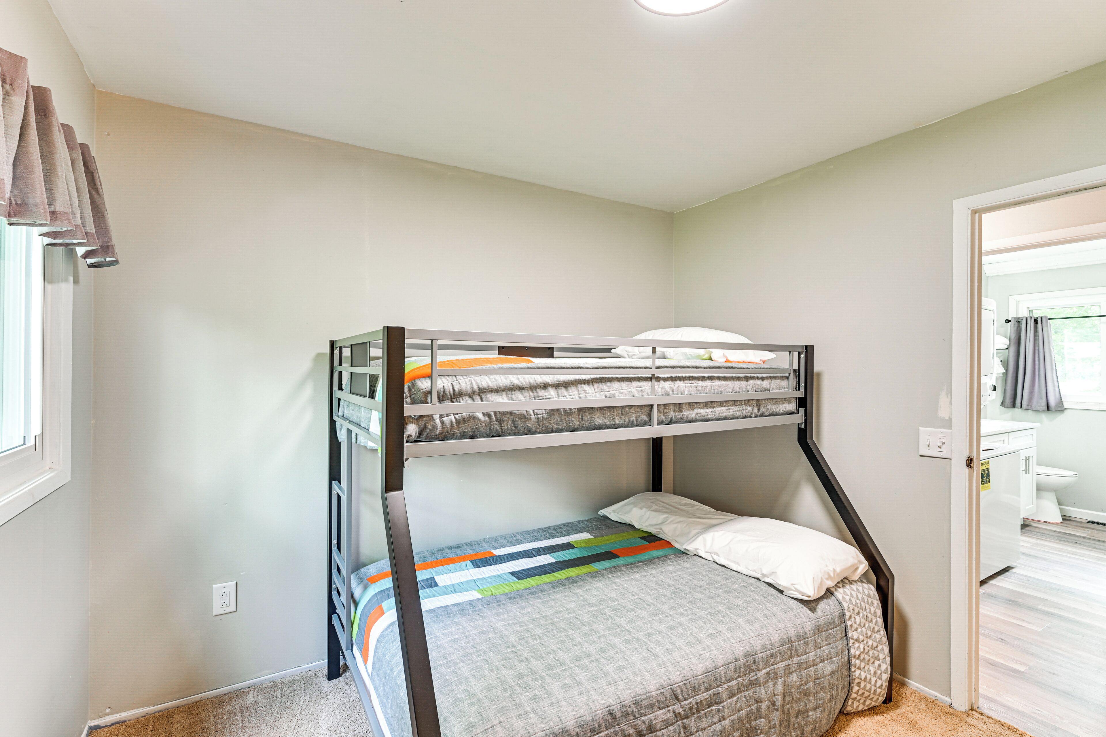 A bunk bed room with a window, a door leading to a bathroom, and a carpeted floor.