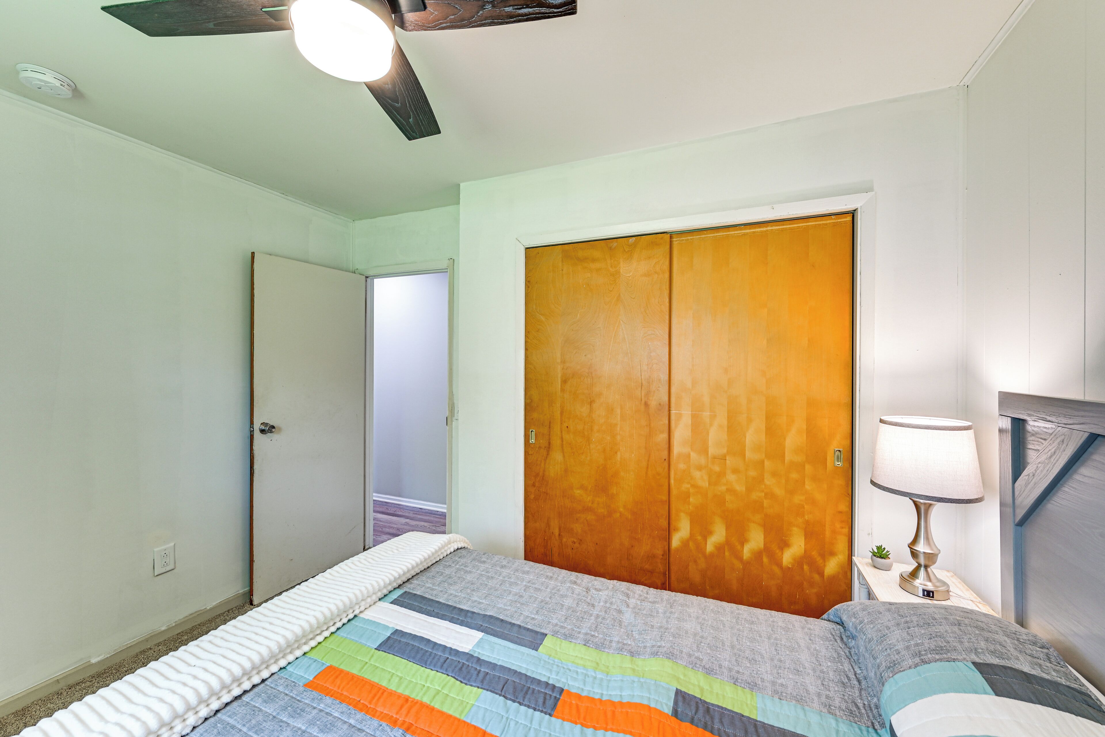 A bedroom with a bed, a wooden wardrobe, a nightstand with a lamp, and a ceiling fan.