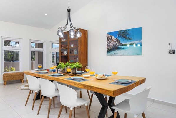 A modern dining area with a wooden table, white chairs, and a chandelier.