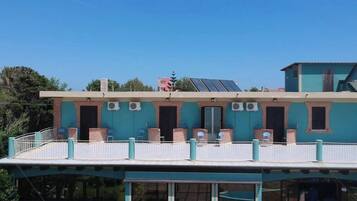 Un edificio de dos pisos con balcón, unidades de aire acondicionado y paneles solares.