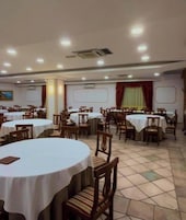 Un salón de conferencias con varias mesas redondas y sillas, manteles blancos y piso de baldosas.