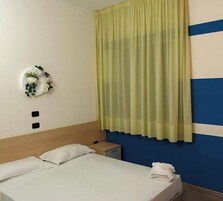 Una habitación de hotel con cama, mesita de noche, teléfono fijo en la pared y un adorno mural.