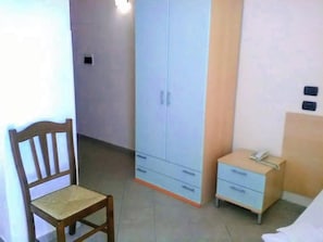 A bedroom with a wooden chair, a wardrobe, a bedside table with a phone, and a bed. - Hotel Baia Mare Blu  (Isola di Capo Rizzuto)