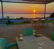 Un área de comedor al aire libre con una mesa dispuesta para dos, con vista a un cuerpo de agua durante la puesta de sol.