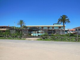 Un edificio costero con entrada techada, palmeras y un área cercada.