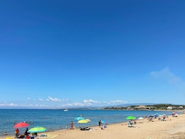 Una playa con gente tomando el sol y nadando, sombrillas de colores y un cielo azul despejado.