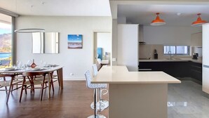 Una cocina moderna con una isla central, un comedor con una mesa redonda y sillas, y vistas al exterior.