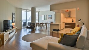 Una sala de estar moderna con un sofá, una televisión y una zona de comedor con sillas y una mesa.
