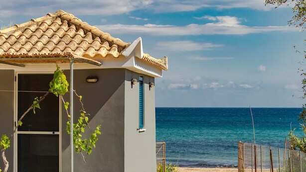 A small building with a tiled roof and a window with blue shutters, located near a beach with a clear view of the sea. - Beach House Steps Away From the sea (Pylos-Nestoras)