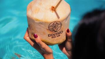 Una persona sostiene un coco con una pajita, con la etiqueta 'DIVINO GILI AIR' en una piscina.
