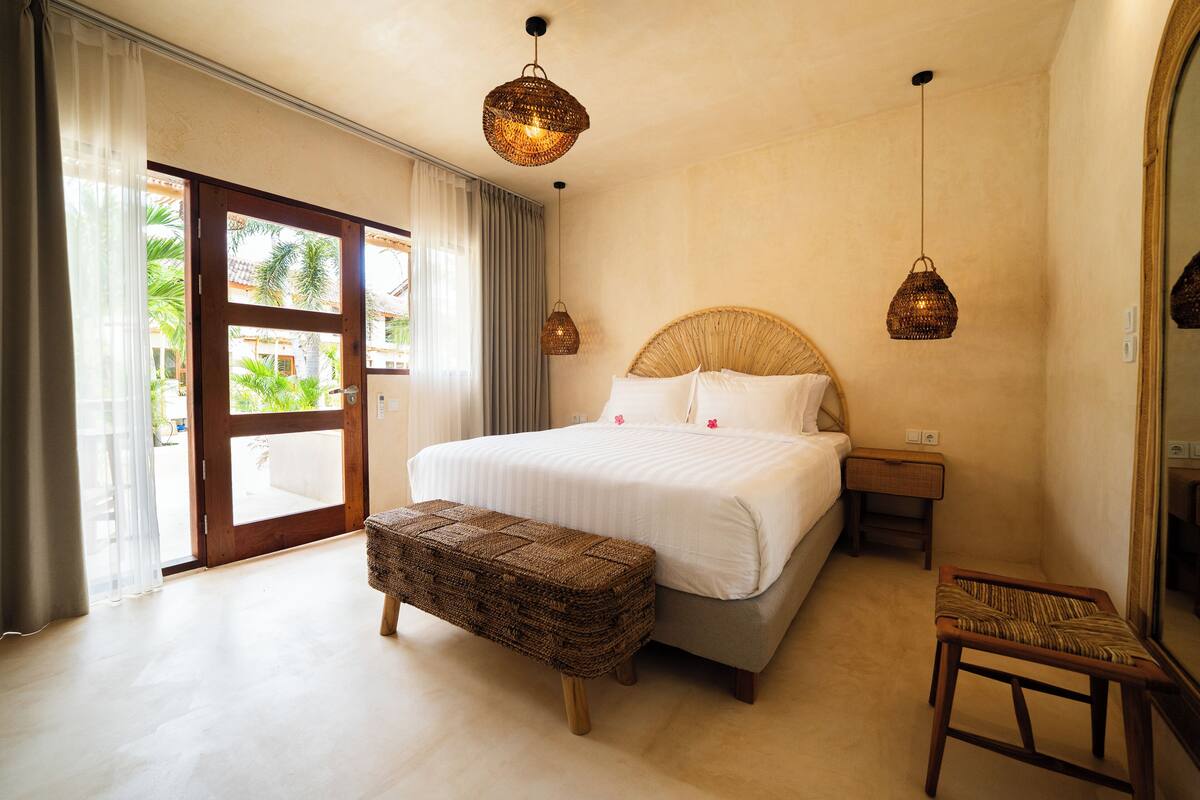 A bedroom with a large bed, a wooden bench, two bedside tables, and a large mirror.