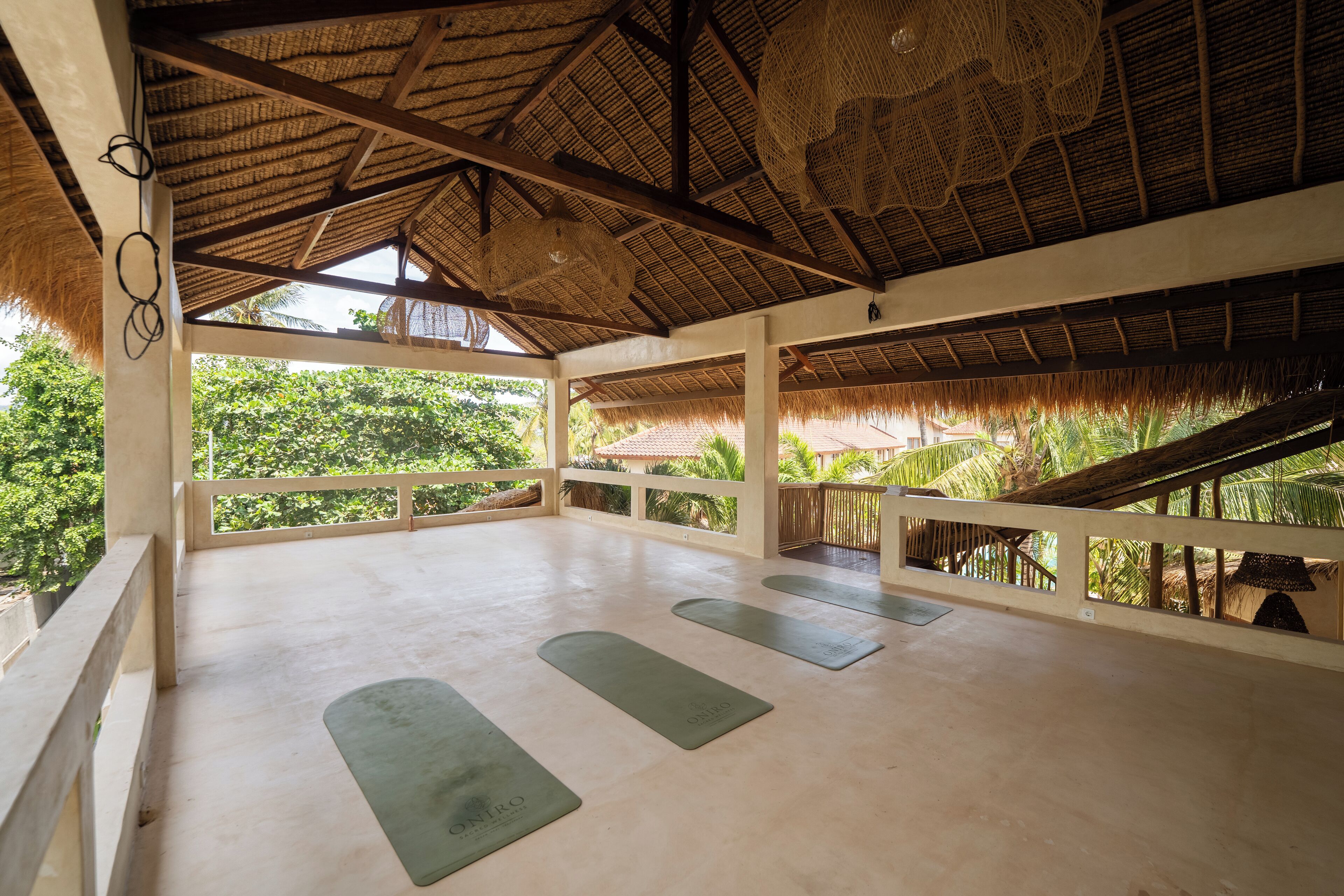 A spacious room with a thatched roof, a balcony with a railing, and a view of lush greenery.