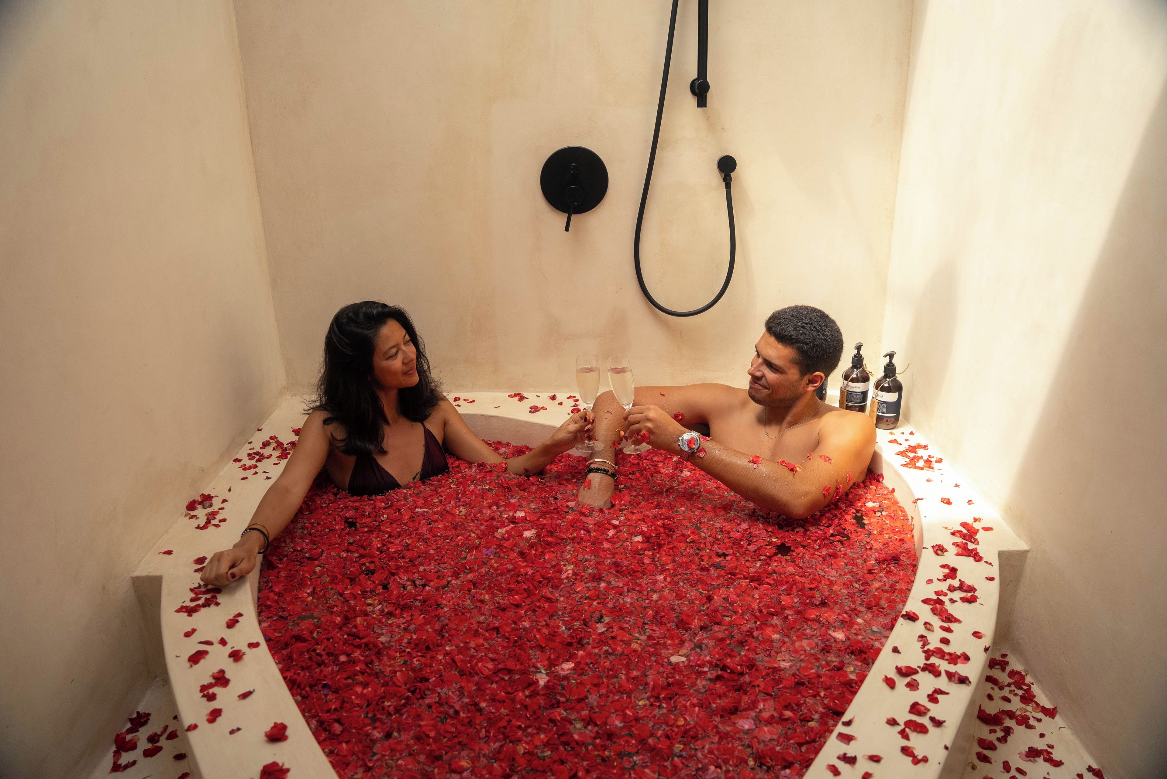 A bathtub filled with rose petals and two people sitting in it.