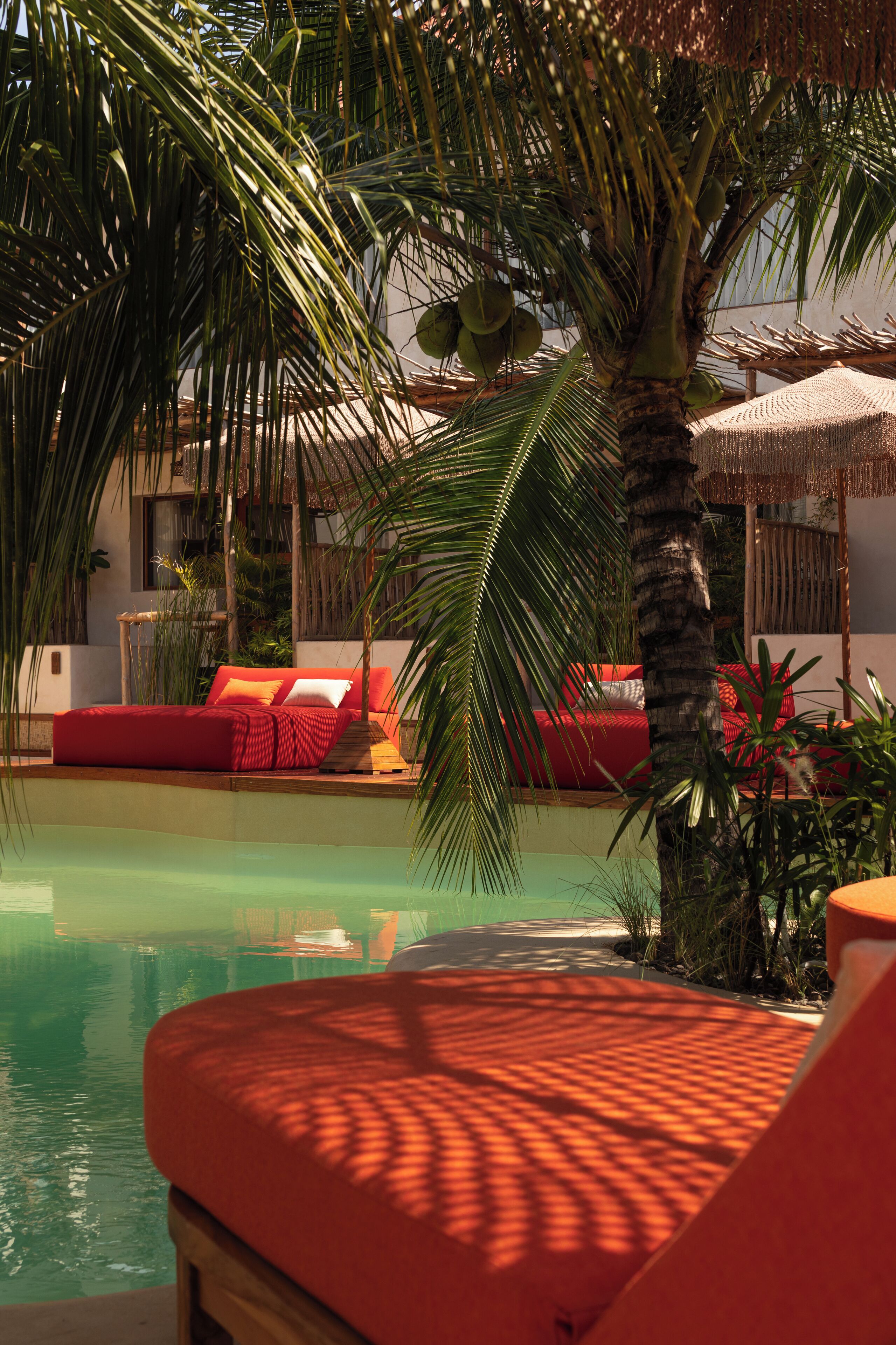A poolside area with a red lounge chair, a palm tree, and a red sofa with cushions.